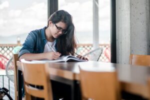 Graduate student writing in a notebook at a sunlit study table