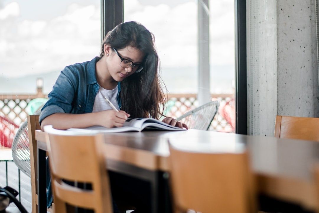 Graduate student writing in a notebook at a sunlit study table