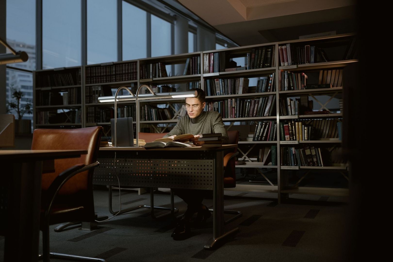Graduate researcher reading at a desk in a quiet, book-filled library